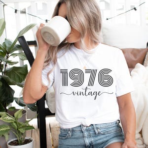 May include: White t-shirt with black text that reads "1976 vintage" in a retro font.
