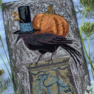 Puede incluir: Patrón rectangular de aguja perforadora con un cuervo negro con sombrero de copa, con una calabaza naranja en el fondo. El diseño incluye el texto "Punch Needle Pattern" y "Embroidery floss pattern". Las dimensiones son 12,7 cm x 20,3 cm.