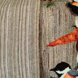 May include: A close-up of a beige and brown striped rug with a colorful needlepoint design featuring a snowman and birds. The snowman has a carrot nose and a black top hat. The birds are brown, blue, and white.