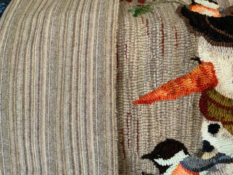 May include: A close-up of a beige and brown striped rug with a colorful needlepoint design featuring a snowman and birds. The snowman has a carrot nose and a black top hat. The birds are brown, blue, and white.