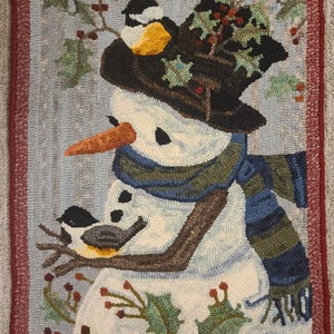 May include: A white snowman with a black hat and a blue and green scarf. The snowman is surrounded by green holly with red berries. Two small black and yellow birds are perched on branches.