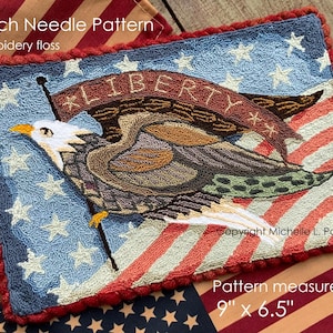 May include: A patriotic punch needle pattern featuring an eagle holding a banner with the word "LIBERTY". The design includes a blue background with white stars and red and white stripes. The pattern measures 9" x 6.5".