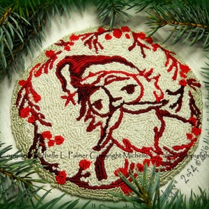Pode incluir: Um ornamento redondo de feltro cor creme com um desenho bordado em vermelho e marrom de uma rena estilizada com bagas de azevinho. O ornamento tem o texto "Copyright Michelle L. Palmer Copyright Michelle L. Palmer Copyright 2014" ao redor da borda.