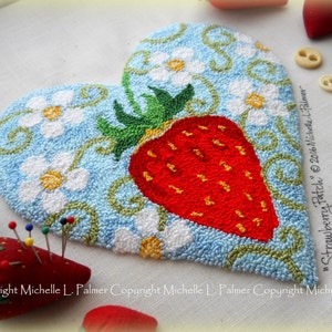 Könnte beinhalten: Ein herzförmiges Nadelbild mit einer roten Erdbeere mit grünen Blättern und weißen Blüten auf blauem Hintergrund. Das Design ist von einem grünen Rankenmuster umgeben. Der Text "Strawberry Patch" und "© 2016 Michelle L. Palmer" ist in der rechten unteren Ecke sichtbar.