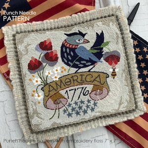 May include: A square punch needle pattern with a bird, flowers, and the word "AMERICA" on a banner, with the year "1776". The pattern is 7" x 7" and includes embroidery floss. The text "Punch Needle PATTERN" is at the top.