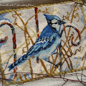 Op de afbeelding: Een blauwe vogel, een blauwe gaaien, met een witte kop en zwarte markeringen zit op een tak met bruine en gele twijgen. De achtergrond is lichtblauw en wit met een rode en witte snoepstok. De afbeelding heeft de titel "Punch needle with Embroidery Floss" en de tekst "Copyright Michelle L. Palmer" onderaan.
