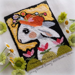 May include: A white bunny with a colorful flower crown, surrounded by pink and green flowers, on a black background with a yellow border. The text "Spring Bonnet Bunny" and "Copyright Michelle L. Palmer" are visible in the bottom right corner.
