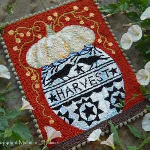 May include: A white pumpkin sits in a blue and white ceramic jar with the word "HARVEST" written on it. The jar is surrounded by a red background with a green vine and yellow berries.