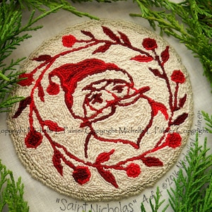 May include: A hand-stitched wool rug featuring a red and white illustration of Santa Claus's face surrounded by a wreath of red berries and leaves. The rug is labelled "Saint Nicholas" and "4 of 2016".