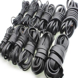 May include: A collection of eleven individual coils of black leather cord arranged in two rows. The top row features thinner, round-profile cords, while the bottom row consists of wider, flat-profile leather strips, all neatly wound into circular bundles.