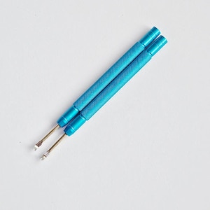 May include: Two blue metal tools with textured handles and thin, silver-coloured tips. The tools are angled diagonally across a white background. The handles are a bright, solid blue colour.