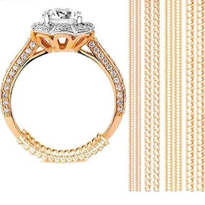 Puede incluir: Un anillo de compromiso de oro con una piedra central grande y transparente y piedras más pequeñas engastadas alrededor. La banda también está adornada con pequeñas piedras. A la derecha del anillo se muestran varios extensores de cadena dorados.