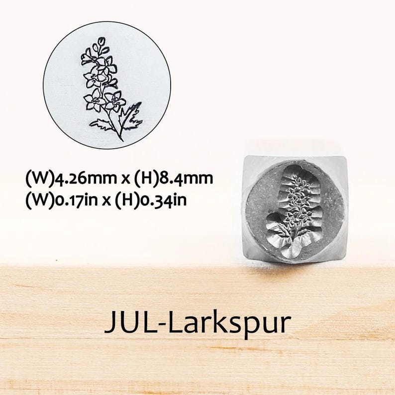Pode incluir: Um carimbo de metal com um desenho floral de espargos. O carimbo tem 4,26 mm de largura e 8,4 mm de altura. O texto "JUL-Larkspur" est&aacute; impresso abaixo.