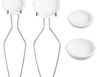 May include: Two white ceramic crucibles with metal handles, and two additional white ceramic crucibles. The crucibles are used for melting and heating materials in a laboratory setting.