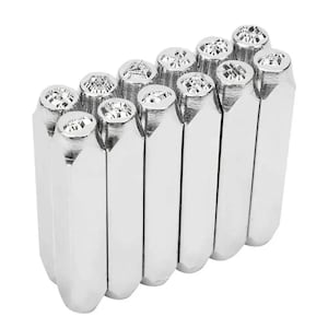 May include: A set of twelve silver metal stamps with various decorative designs on the stamp heads. The stamps are arranged in a neat, vertical row, with the stamp heads facing upwards. The designs include geometric shapes and patterns.