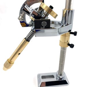 May include: A chrome and brass jewelry making tool with a rotating arm and a protractor. The tool is mounted on a chrome base.