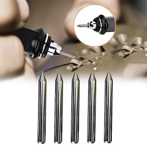 May include: A black rotary tool with a silver tip is shown in use, with a close-up inset. Below, five silver engraving tips are displayed, each with a pointed end. The tools appear to be for detailed carving or engraving.