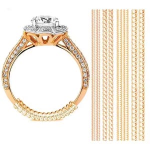 Puede incluir: Un anillo de compromiso dorado con una piedra preciosa grande y transparente en el centro y piedras más pequeñas a lo largo de la banda. El anillo va acompañado de varios ajustadores de tamaño de anillo.