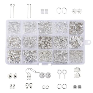 Op de afbeelding: Een doorzichtige plastic organizer gevuld met diverse zilverkleurige sieradencomponenten. De collectie bevat kopspelden, oogstiften, sprongringen, oorhaakjes en decoratieve kralen. Ideaal voor het maken van oorbellen, kettingen en armbanden.