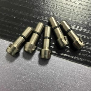 May include: Five small, metallic cylindrical pins with a smooth, polished finish. Each pin features a distinct notched head and a thin, black rubber O-ring positioned around the upper portion of the shaft, designed for secure fitting and alignment.