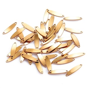 May include: A collection of small, gold-colored, oval-shaped metal tags with a hole at each end. The tags are scattered across a white surface, reflecting light and appearing shiny. These tags are suitable for jewelry making or crafting.