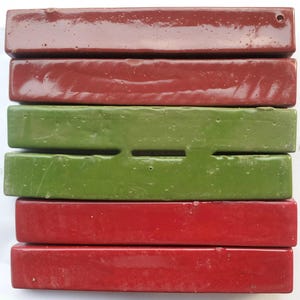 May include: A stack of six rectangular ceramic tiles in shades of red and green. The top tile is a dark maroon, followed by a red tile, then two green tiles, and finally two more red tiles. One green tile has a rectangular cutout.