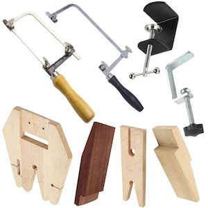 May include: A collection of jewelry-making tools, including hand saws with wooden and black handles, clamps, and wooden forming blocks. The tools are designed for precision work and are displayed against a white background.