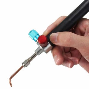 Puede incluir: Un soplete de mano negro y plateado con una perilla roja y azul. El soplete tiene una punta de cobre y se sostiene en una mano.