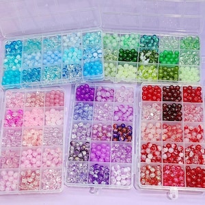 Peut inclure: Assortiment de perles colorées dans des boîtes de rangement en plastique transparent. Les perles sont de différentes nuances de bleu, vert, rose, violet et rouge. Les perles sont rondes et semblent être en verre ou en acrylique. Idéal pour la création de bijoux et l'artisanat.