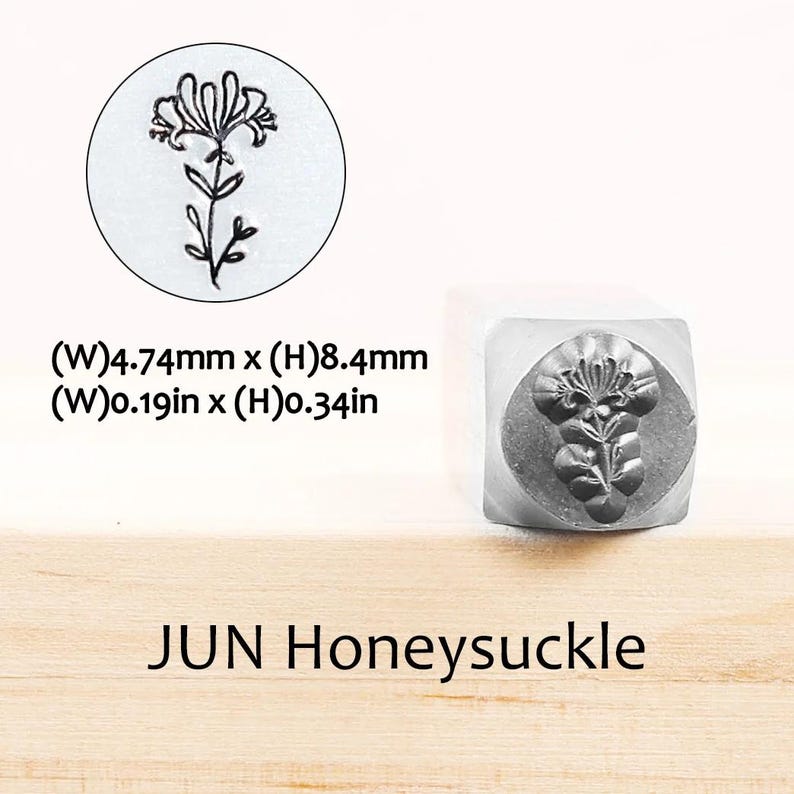 Pode incluir: Um carimbo de metal com um desenho de madressilva. O carimbo tem uma pega quadrada e uma impress&atilde;o circular de uma flor de madressilva. O texto "JUN Honeysuckle" est&aacute; abaixo. O carimbo tem 4,74 mm de largura e 8,4 mm de altura.