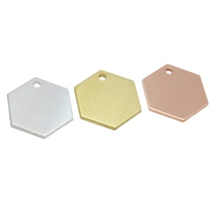May include: Three flat, hexagonal metal tags arranged in a row. The first tag is silver-coloured, the second is gold-coloured, and the third is copper-coloured. Each tag features a single small circular hole punched near the top edge for attachment.