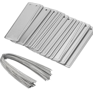 May include: A collection of rectangular, silver metal tags with a small hole at the top, stacked in a pile. A bundle of silver wire is in the foreground. The tags have a slightly raised border.