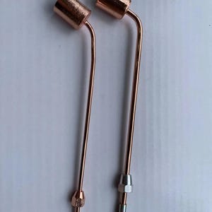 Op de afbeelding: Twee koperkleurige metalen buizen, elk met een cilindrische kop aan de bovenkant en een lange, gebogen steel. De linkerbuis heeft een bijpassend koperkleurig hulpstuk aan de basis, terwijl de rechterbuis een zilverkleurig hulpstuk heeft.
