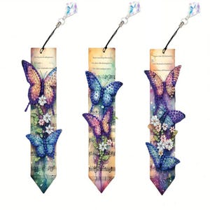 May include: Three butterfly-themed bookmarks with watercolour backgrounds and musical notes. Each bookmark features butterflies in shades of purple, blue, and yellow, with floral accents. A crystal charm is attached to each bookmark.