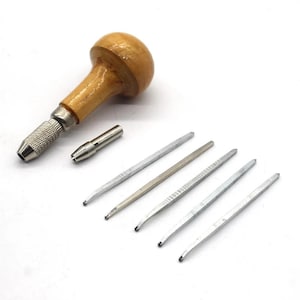 Op de afbeelding: Een set houtsnijgereedschap, waaronder een houten handvat met een metalen boorkop, een kleine metalen boor en vijf metalen snijgereedschappen met verschillende puntvormen. De gereedschappen zijn gerangschikt op een wit oppervlak.