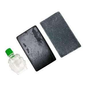 May include: A clear glass bottle with a green cap and two rectangular, dark gray stones. One stone is a darker shade of gray than the other. The bottle contains a clear liquid.