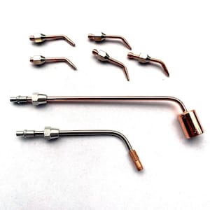 May include: A collection of welding torch tips and components. The image shows several small, curved tips with a copper finish, along with two larger torch bodies. The torches have a copper and silver finish, and are arranged on a white background.