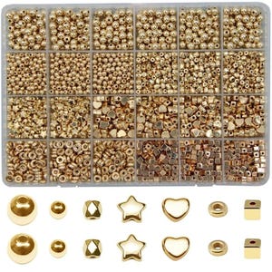 May include: A clear plastic organiser filled with various gold-coloured beads and charms. The beads are in different shapes and sizes, including round, heart, star, and square. The organiser is divided into multiple compartments.