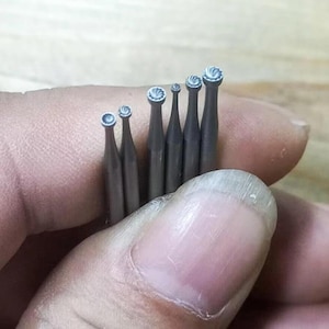 May include: A set of seven small, silver-coloured metal tools with rounded tips. The tools are held in a hand, and the tips are all facing the camera.