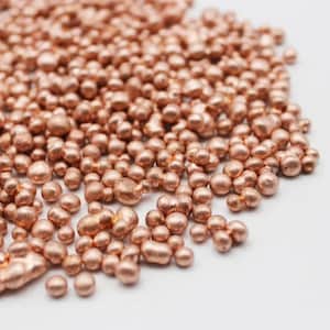 May include: A close-up shot of numerous small, copper beads. The beads are of varying sizes and shapes, with a shiny, metallic surface. The colour is a warm reddish-brown, with highlights and shadows. The beads are scattered on a white background.