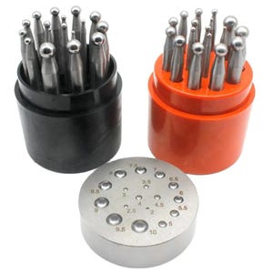 Könnte beinhalten: Ein Set aus Metall-Kugelpolierwerkzeugen mit kugelförmigen Spitzen, angeordnet in einem schwarzen und einem orangefarbenen zylindrischen Behälter, sowie einem runden Metallsockel mit nummerierten Vertiefungen von 2 bis 10.