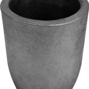 Pode incluir: Um cadinho cilíndrico cinza com uma abertura larga e um fundo arredondado. O recipiente de metal tem uma superfície texturizada e é projetado para suportar altas temperaturas. O cadinho é usado para derreter substâncias.