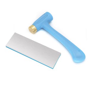 Könnte beinhalten: Ein hellblauer Hammer mit einem goldfarbenen Metallkopf und ein rechteckiger Metall-Amboss mit einer gebürsteten silbernen Oberfläche und einer blauen Basis. Das Werkzeugset ist für Metallbearbeitung und Schmuckherstellung gedacht.