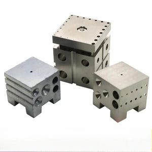 May include: Three silver metal blocks of varying sizes. The largest block is a cube with a rectangular top and multiple drilled holes. The other two blocks are also cube-shaped, with holes and cutouts. The blocks are on a white background.