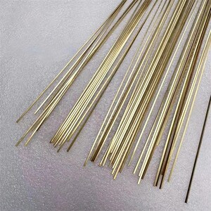 May include: A collection of thin, straight, golden-colored metal rods, possibly brass or similar alloy, arranged in a loose bundle. The rods are of uniform length and diameter, with a smooth, reflective surface. A single, darker rod is also present.