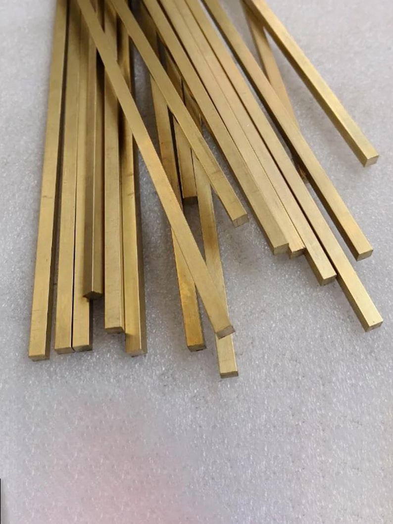 May include: A collection of rectangular brass bars, each with a golden hue. The bars are of varying lengths and are arranged in a scattered pattern. The metal bars are likely for crafting or industrial use.