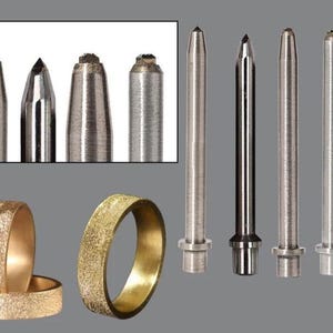 Puede incluir: Una variedad de herramientas y anillos de metal. Las herramientas tienen varias formas de punta, incluyendo cónicas y planas. Los anillos tienen una superficie texturizada de color dorado. El fondo es gris sólido.