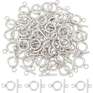 May include: A collection of shiny, silver-colored jewelry clasps, including circular rings and straight bar components. The clasps are of varying sizes and are scattered across the image, with a few arranged in a row at the bottom. These are likely used for jewelry making.