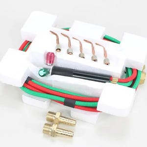 May include: A new welding torch kit, featuring a black handle, copper tips, and red and green hoses. The kit includes brass fittings and is packaged in a white foam insert.