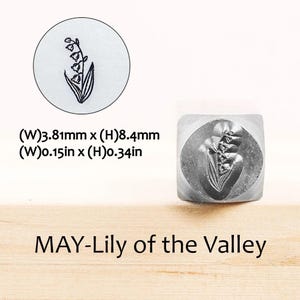 Pode incluir: Um carimbo de metal com um desenho de l&iacute;rio-do-vale. O carimbo &eacute; quadrado com uma imagem floral detalhada. O texto "MAY-Lily of the Valley" est&aacute; abaixo. O carimbo mede 3,81 mm de largura e 8,4 mm de altura.